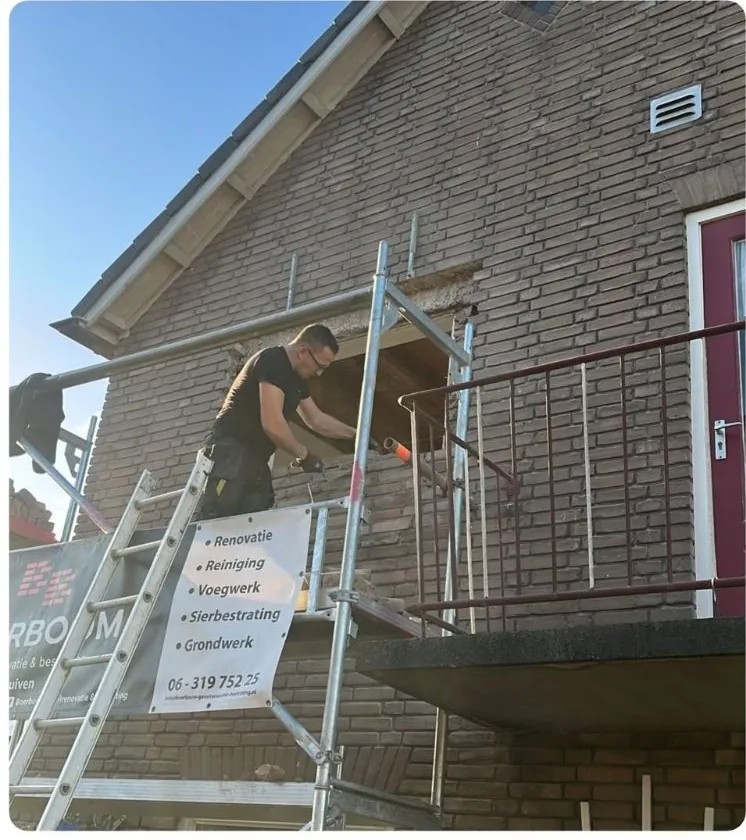 Jeroen aan het werk op de steiger bij een balkon, met het bord van Boerboom