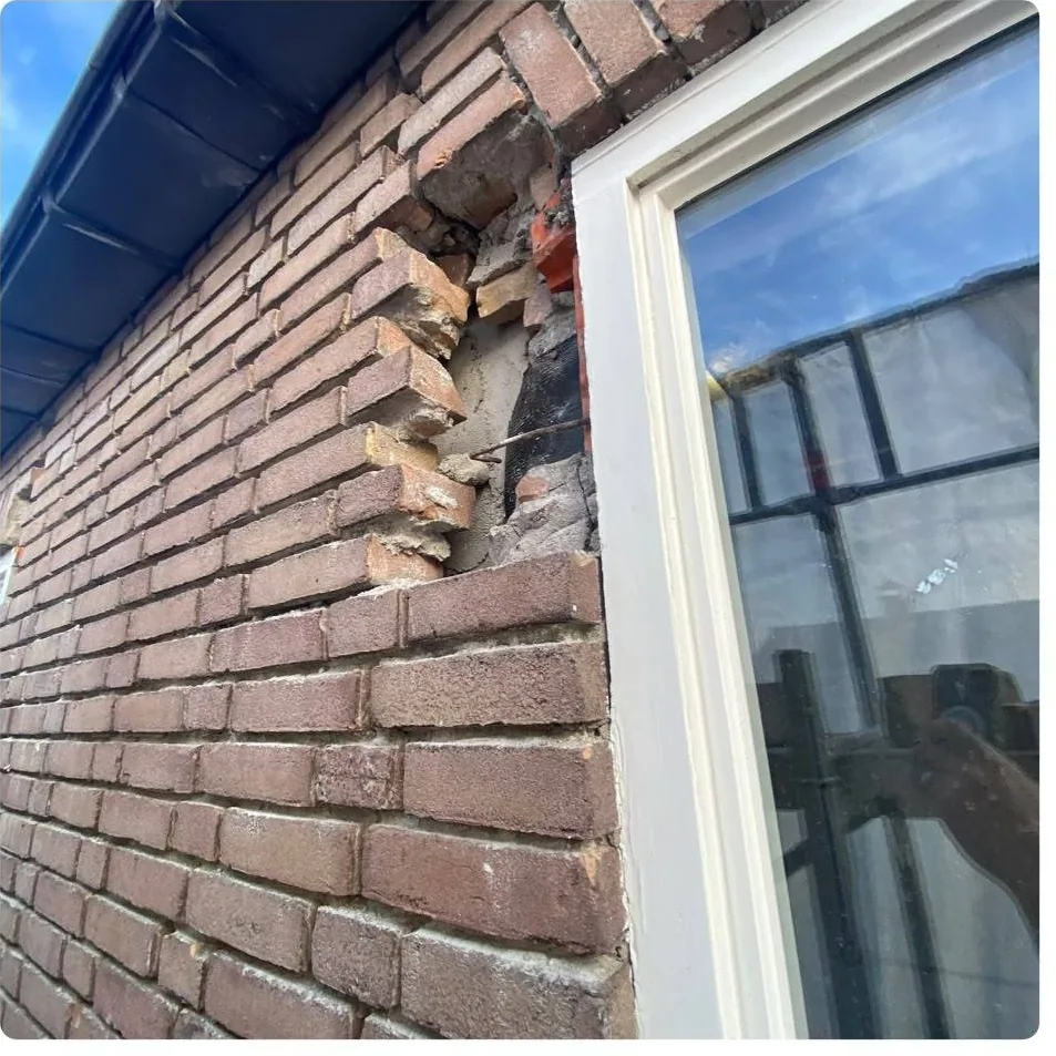 Kapotte en losse stenen in de hoek van een gevel, naast een kozijn