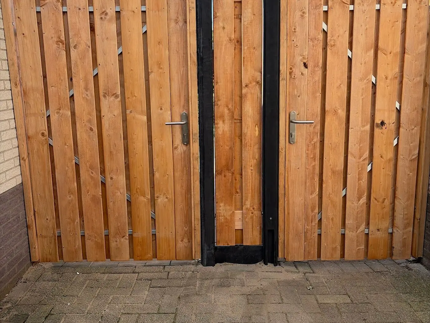 Nieuwe houten schutting met poortdeur naast een woning