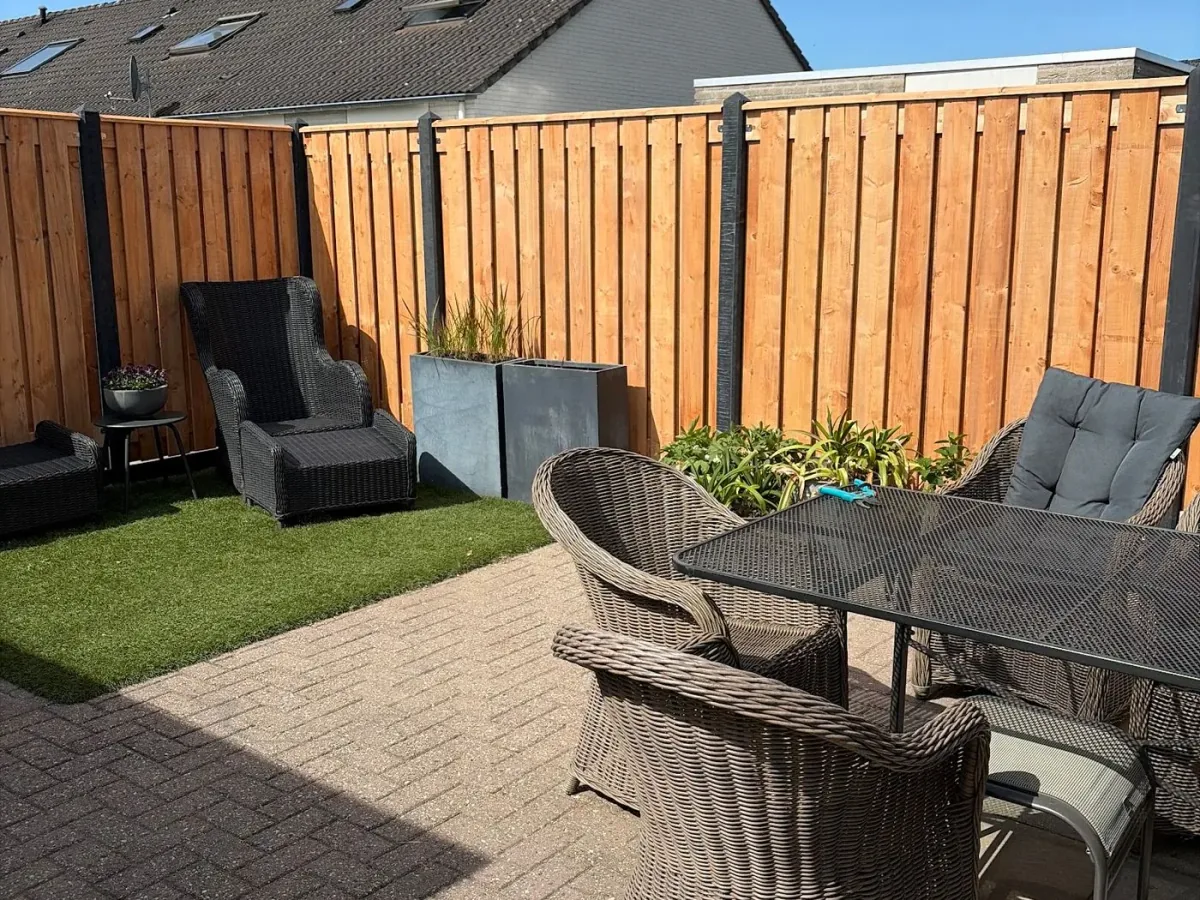 Terras met tuinstoelen, kunstgras en een houten schutting