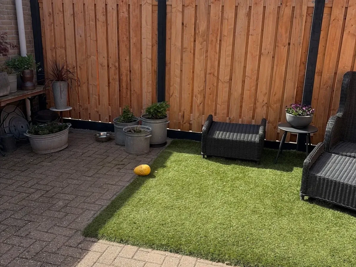 Achtertuin met een houten schutting, kunstgras en klinkers