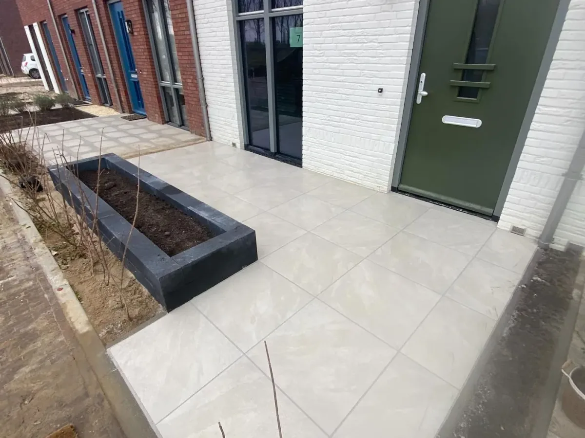 Voortuin met grote keramische tegels en een zwarte plantenbak