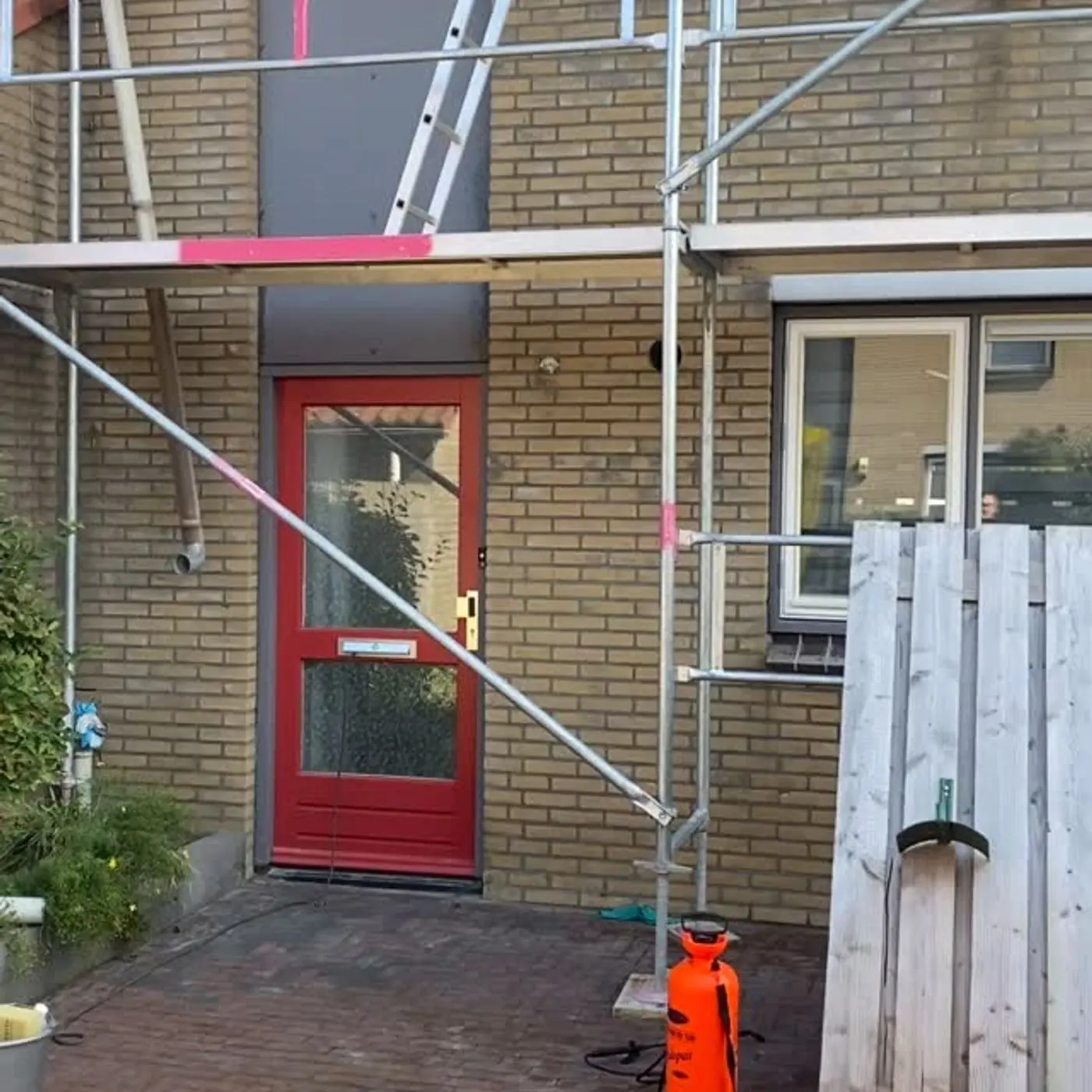 Gevel met rode voordeur, steiger wordt afgebroken na het impregneren