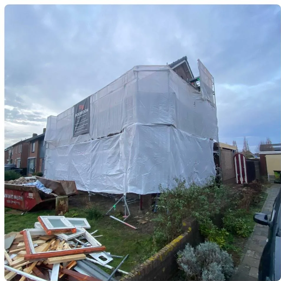 Ingepakte steiger rond een woning, met container en sloopafval op het gras