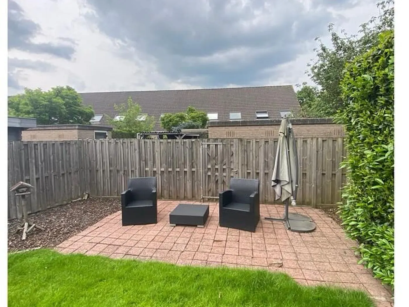 Achtertuin met een bestraat terras, tuinstoelen en strak gazon