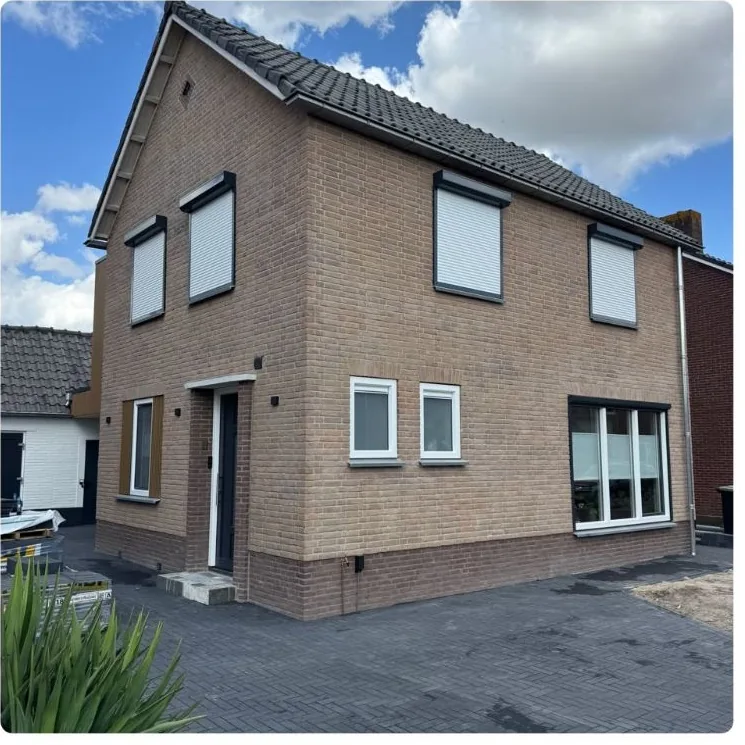 Dezelfde voorkant na de renovatie, met nieuwe kozijnen, rolluiken en bestrating