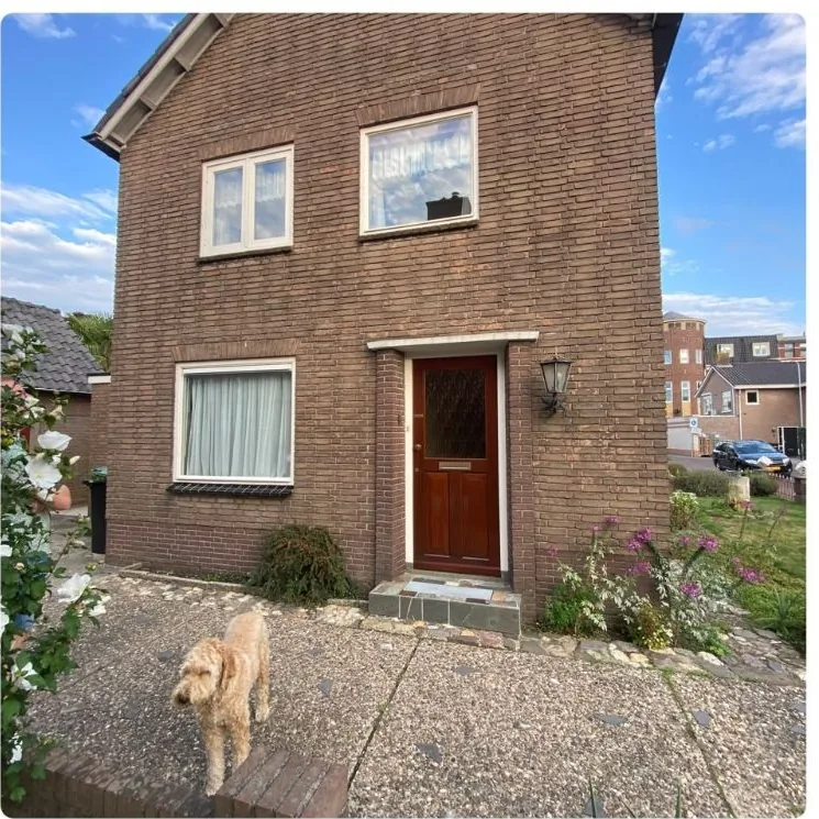 Voorkant van een bakstenen woning met een rode voordeur en grindpad, vóór de renovatie