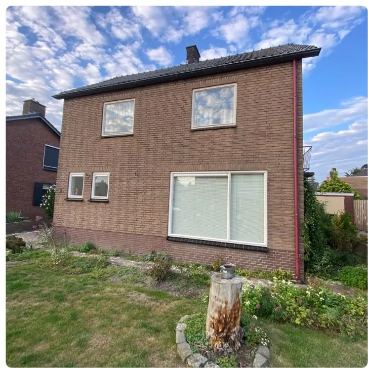 Zijkant van dezelfde woning met een gazon en borders, vóór de renovatie